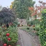 Gartenbereich mit Beeten, Gehölzen und roter Keramikdeko bei Pflanzen Weiglein